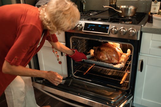 A senior woman checking a roasted turkey in the oven for Thanksgiving preparations.