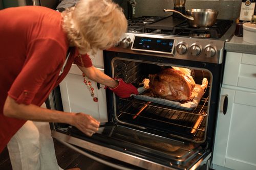 Free A senior woman checking a roasted turkey in the oven for Thanksgiving preparations. Stock Photo