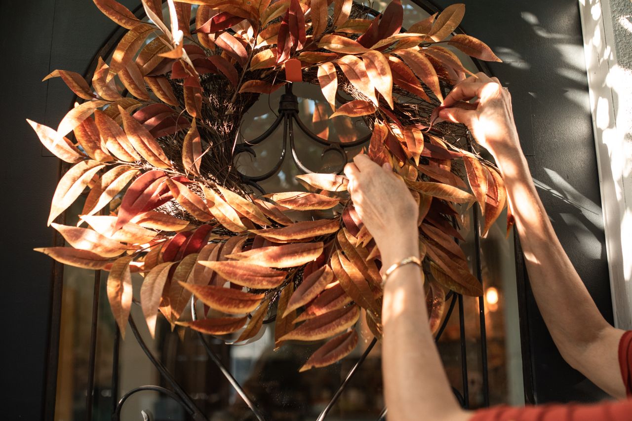 Hands hanging an autumn leaf wreath on a front door