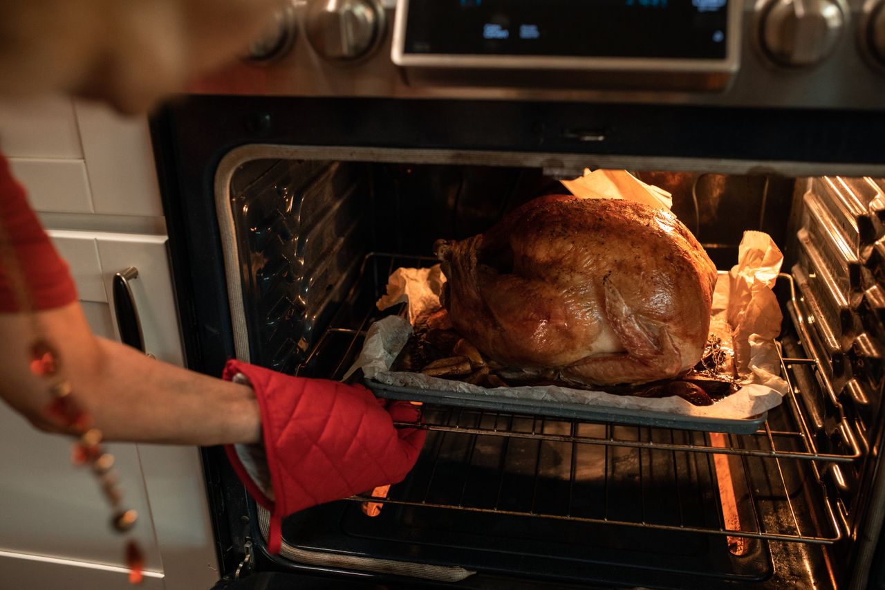 Roasted turkey being pulled from the oven with an oven mitt