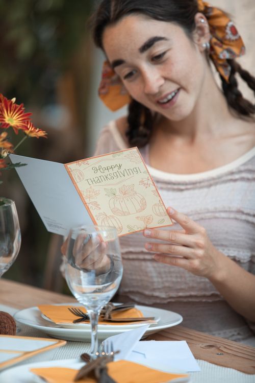 Free A woman enjoys reading a Thanksgiving card at a beautifully set dinner table, capturing the festive holiday spirit. Stock Photo