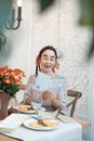 Woman in White Long Sleeve Shirt Sitting on Brown Wooden Chair Holding White Book