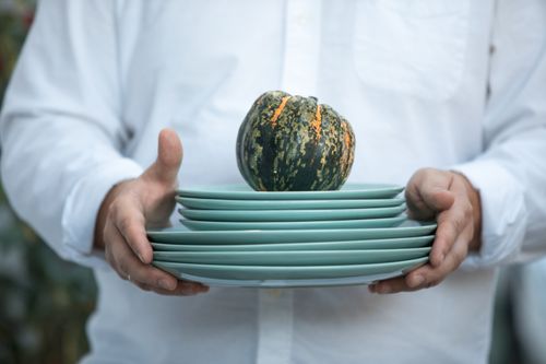 Free Person holding a stack of green plates with a small squash on top, symbolizing fall. Stock Photo