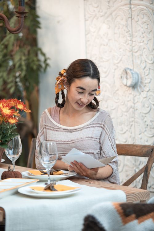 Free Woman reading a note at a Thanksgiving dinner table, enjoying a festive indoor setting. Stock Photo