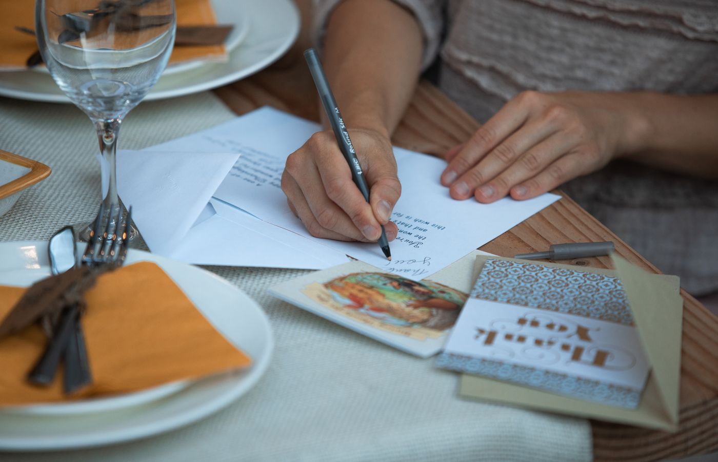 Woman writing thank you notes at a Thanksgiving dinner table setting.