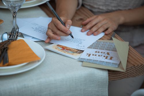 Free A person writing a Thanksgiving thank you note at a dinner table, surrounded by festive decor. Stock Photo