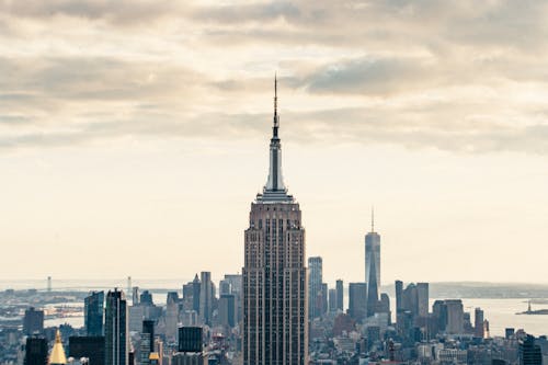 Free Top of skyscraper against modern buildings located in downtown of New York City in USA under cloudy sky highlighted by sunlight Stock Photo