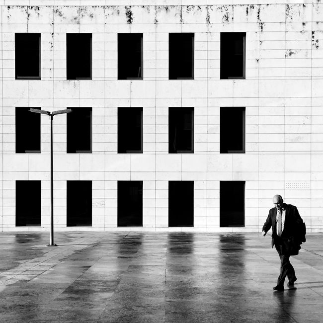 A businessman in Lisbon walks past a modern building in a striking monochrome setting.