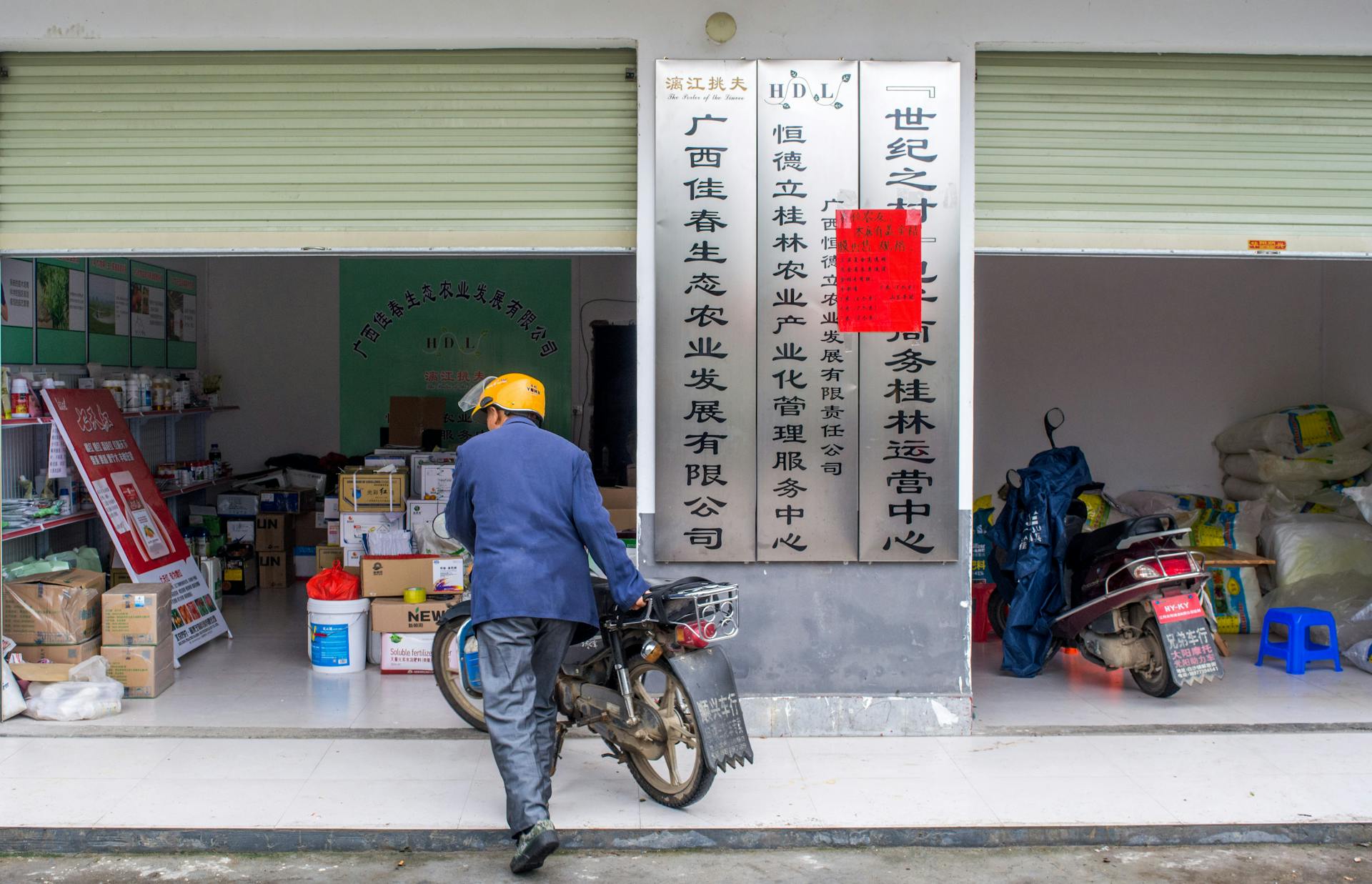 Man pushes motorbike in front of a store in an urban Chinese setting.