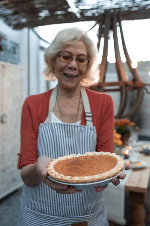 Free Senior woman proudly holds a freshly baked pumpkin pie indoors. Stock Photo