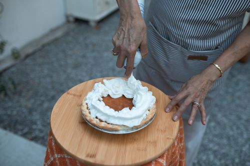 Free Close-up of hands adding whipped cream to a delicious pumpkin pie on a wooden plate. Stock Photo
