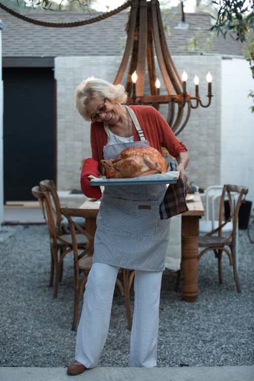 Free Elderly woman in apron holding roasted turkey outdoors during Thanksgiving celebration. Stock Photo