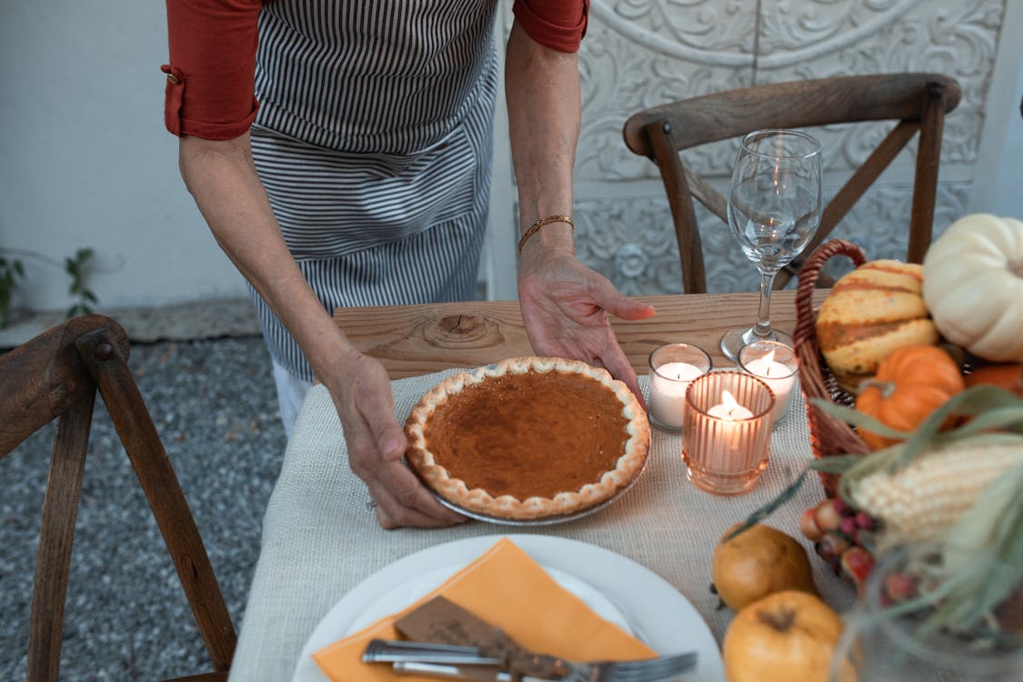 Free Person Placing a Pumpkin Pie on Wooden Table  Stock Photo