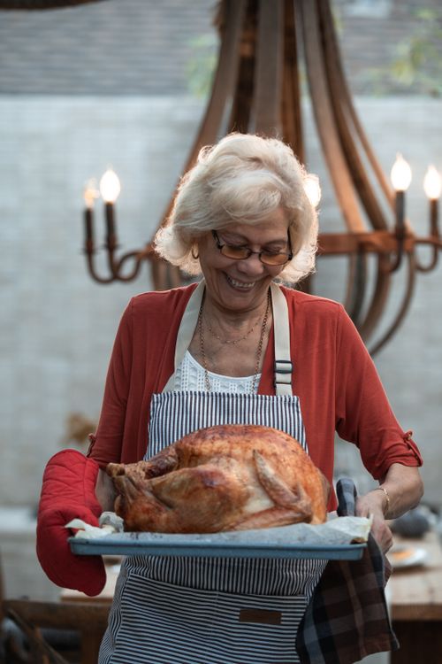 Free Elderly woman holding a roasted turkey, celebrating Thanksgiving indoors. Stock Photo
