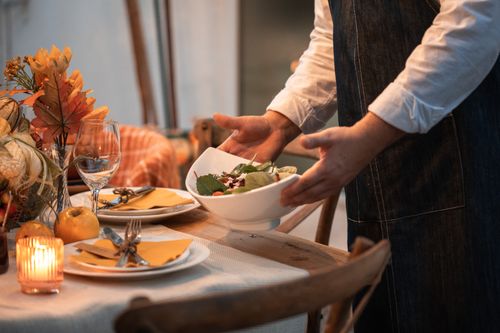 Free Warm and inviting autumn table setting with a person serving salad, perfect for Thanksgiving dinner. Stock Photo