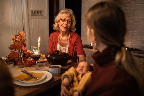 Free Warm indoor family dinner scene with grandmother, mother, and baby at a candlelit table. Stock Photo