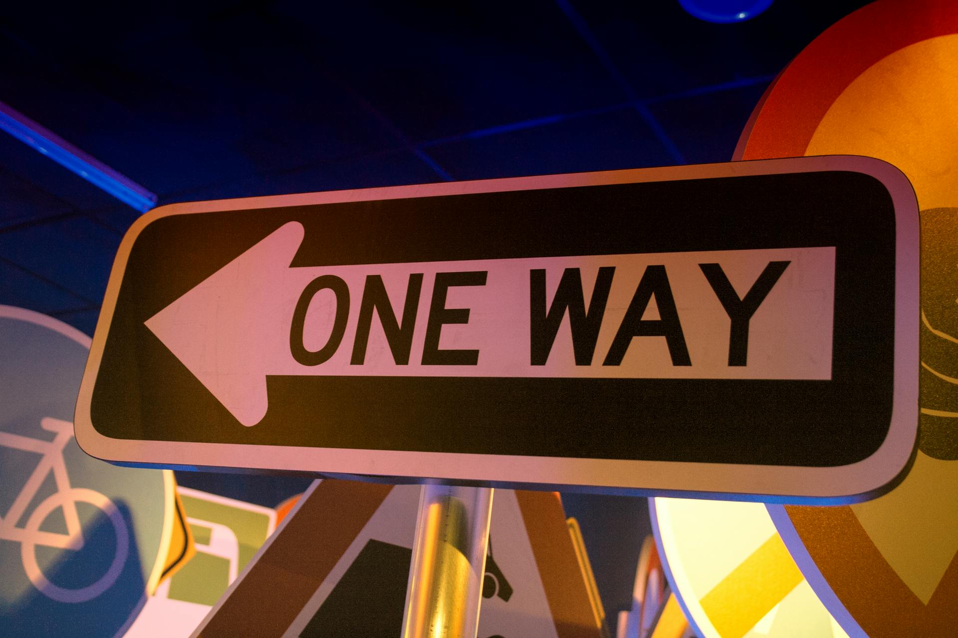 A brightly lit one way street sign with an arrow, captured indoors at night.