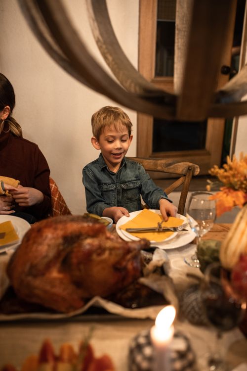 Free Caucasian boy enjoying a Thanksgiving family dinner with roasted turkey and festive setup. Stock Photo