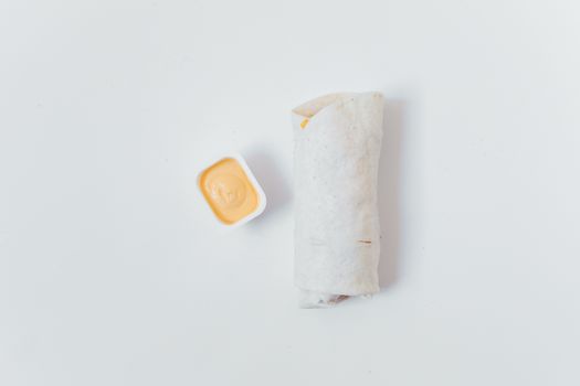 Simple food scene with a burrito and cheese dip on a white surface, perfect for food photography.
