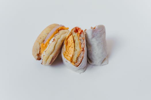 Close-up of tasty breakfast options, a burrito and sandwich, on a white background.