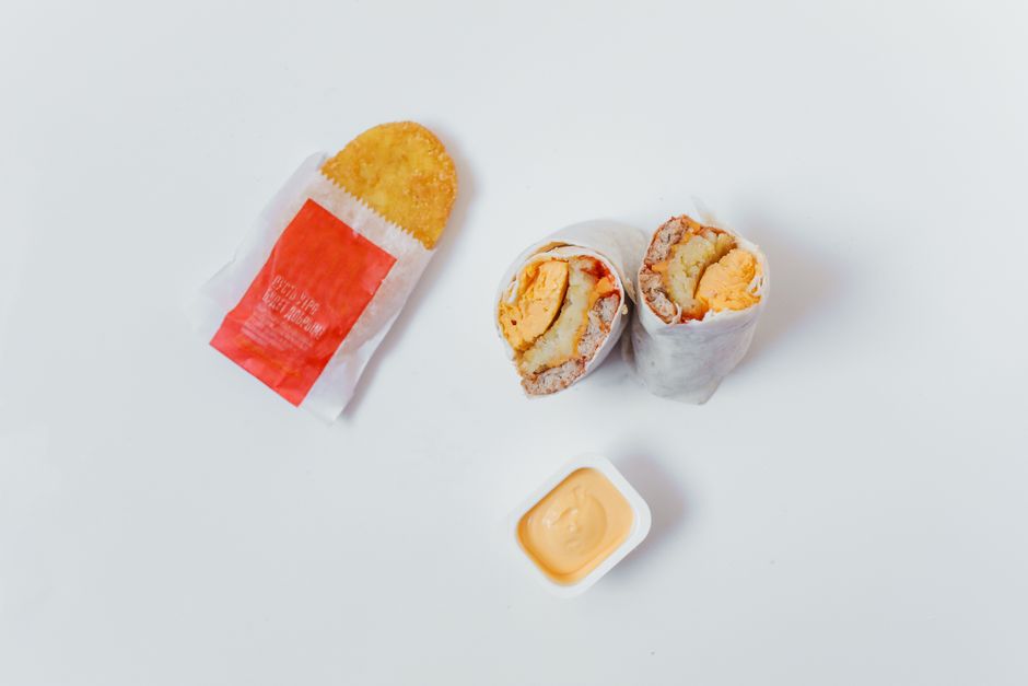Tasty breakfast burrito and hash brown on a plain white background.