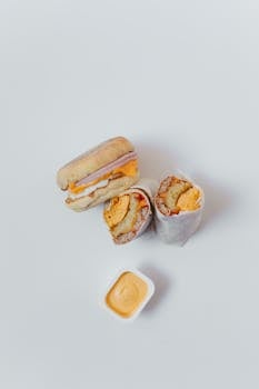 A delicious breakfast burrito and sandwich with sauce on a plain white background, ideal for food presentations.