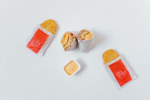 Flat lay of breakfast burrito and hash browns with sauce on white background.