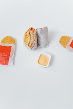 High angle shot of a breakfast burrito, hash browns, and dipping sauce on a white surface.