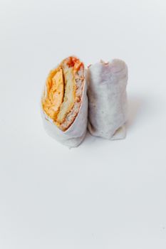 Tasty breakfast burrito filled with cheese and scrambled eggs on a white background.