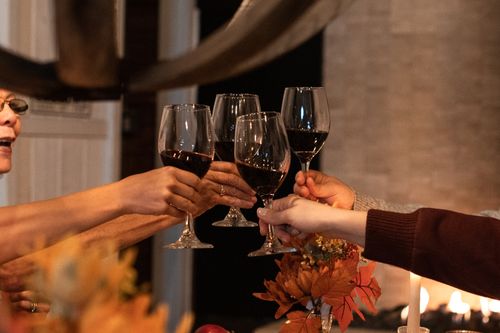 Free A group of people toasting with red wine glasses, celebrating indoors in a warm, cozy atmosphere. Stock Photo