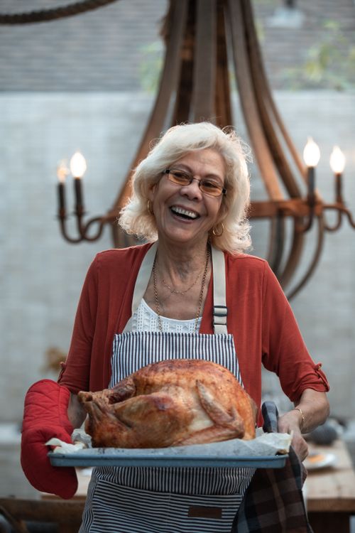 Free Delighted elderly woman in glasses presenting a freshly roasted turkey indoors. Stock Photo