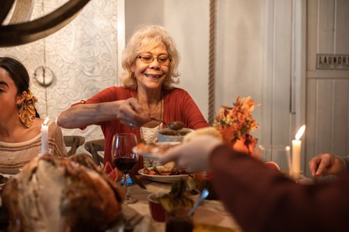 Free Senior woman enjoying a Thanksgiving dinner, sharing hearty meals with family indoors. Stock Photo