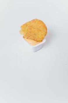 A crispy hash brown partially dipped in creamy sauce on a white surface.