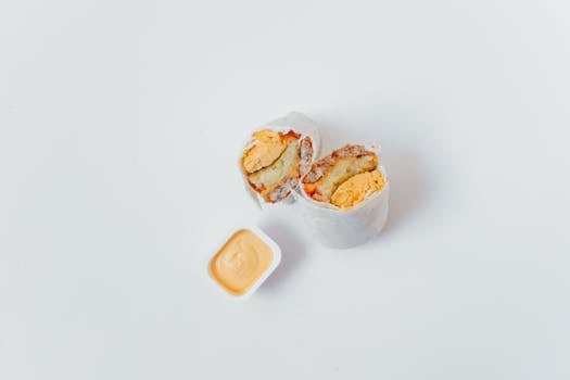 Sliced breakfast burrito with a side of creamy sauce on a clean white surface captured in top view.