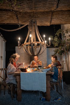 A family enjoys dinner together outdoors under a chandelier, sharing a warm and festive moment.