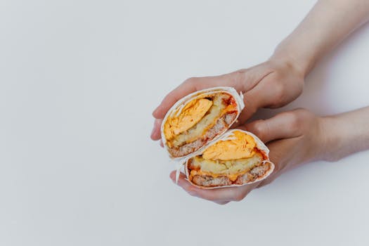 Delicious breakfast burrito with eggs and cheese held by hands.