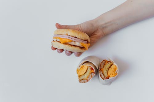 Person Holding Burger Beside Burritos 