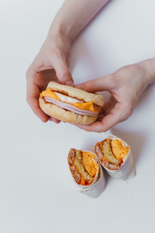 Person Holding Burger Near Burritos 