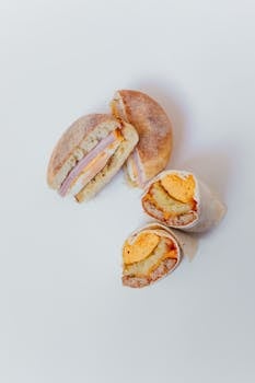 A vertical shot of a breakfast burrito and sandwich on a white background.