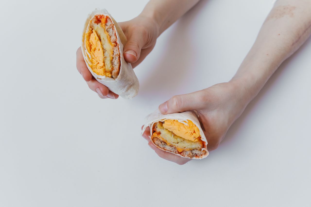 close up of hands holding a cut breakfast burrito with eggs cheese and