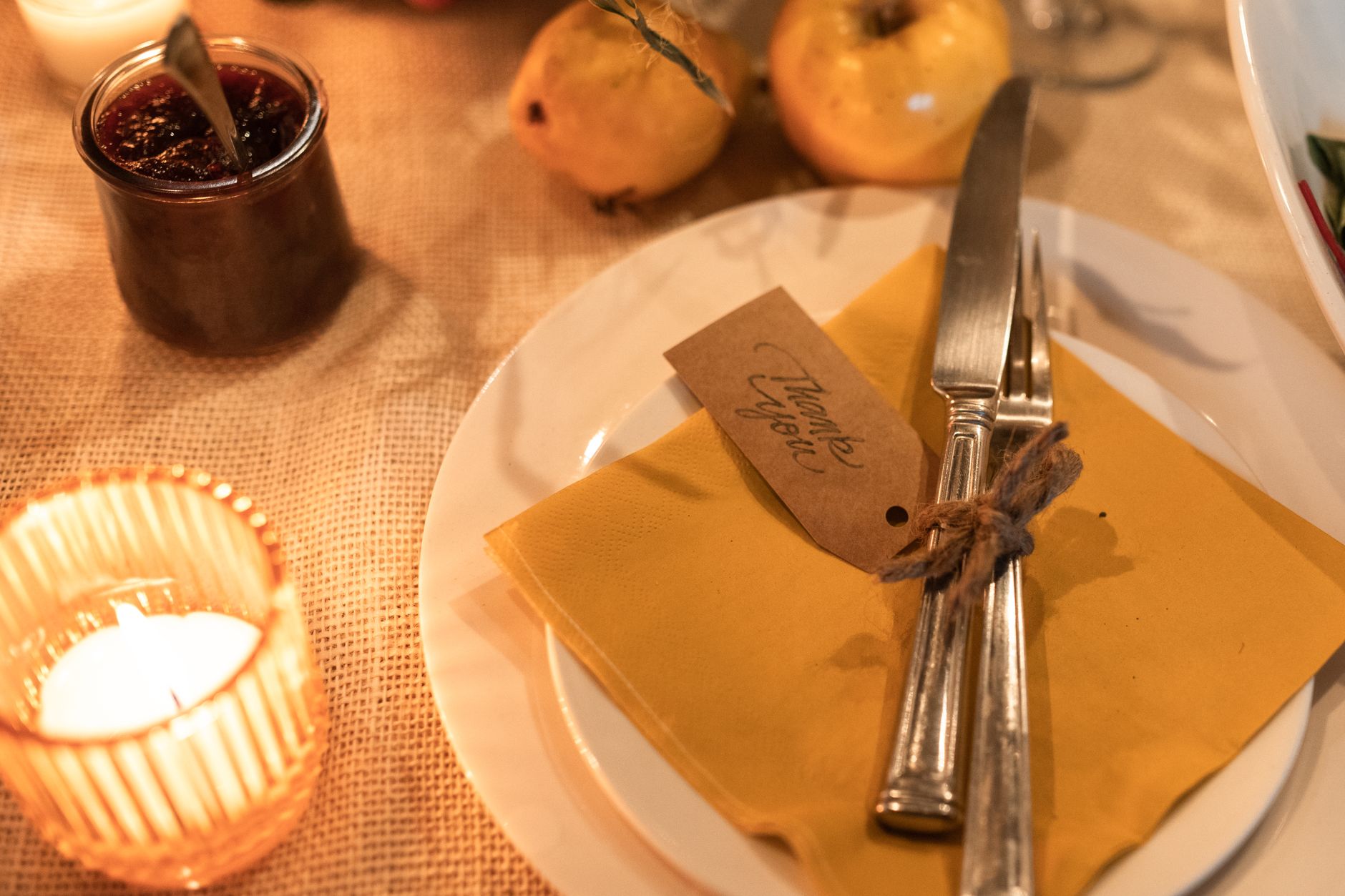 Warm and inviting table setting featuring cutlery, candle, and thank you note.