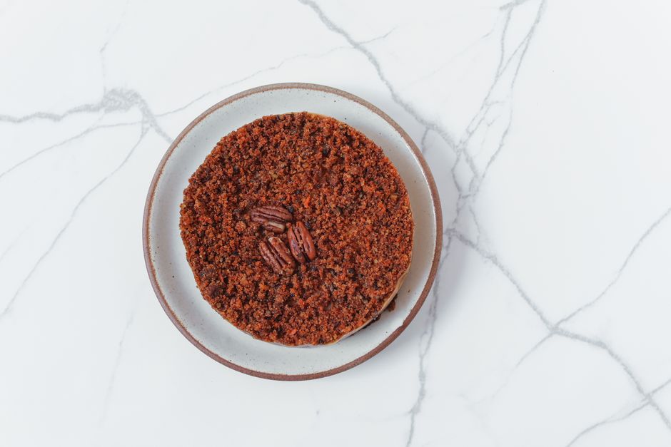 A baking dish of mashed sweet potato casserole topped with golden toasted oats and chopped pecans, served in a white ceramic dish.