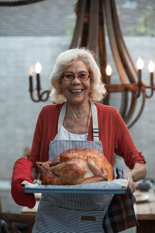 Free Happy elderly woman proudly presenting a roasted Thanksgiving turkey indoors. Stock Photo