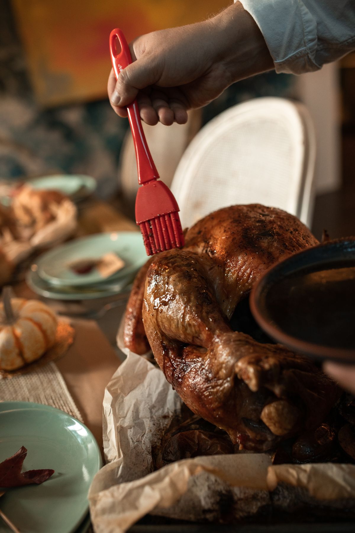 Hands basting a whole roasted turkey in a pan after a fridge thaw that dodged one of the classic Thanksgiving hosting mistakes