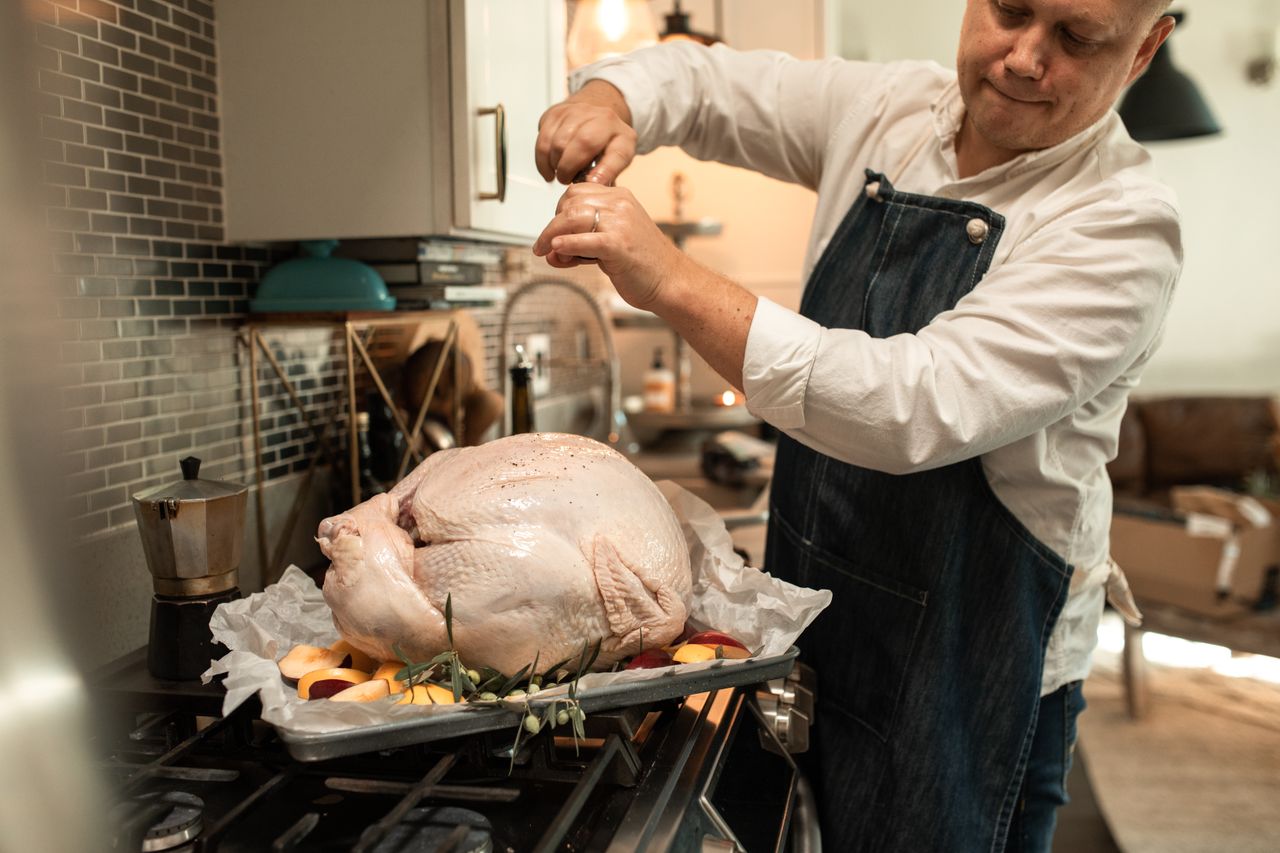 Man seasoning a raw whole turkey in a kitchen