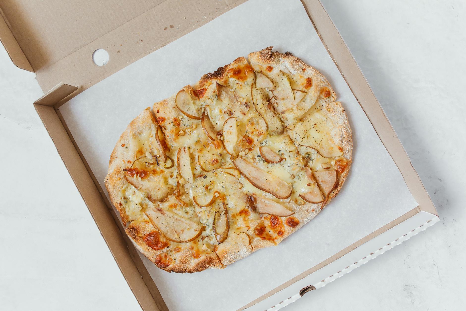 Delicious gourmet pizza topped with pear and cheese, presented in a pizza box.
