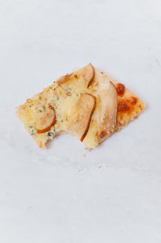A mouthwatering slice of pear and blue cheese pizza against a white background.