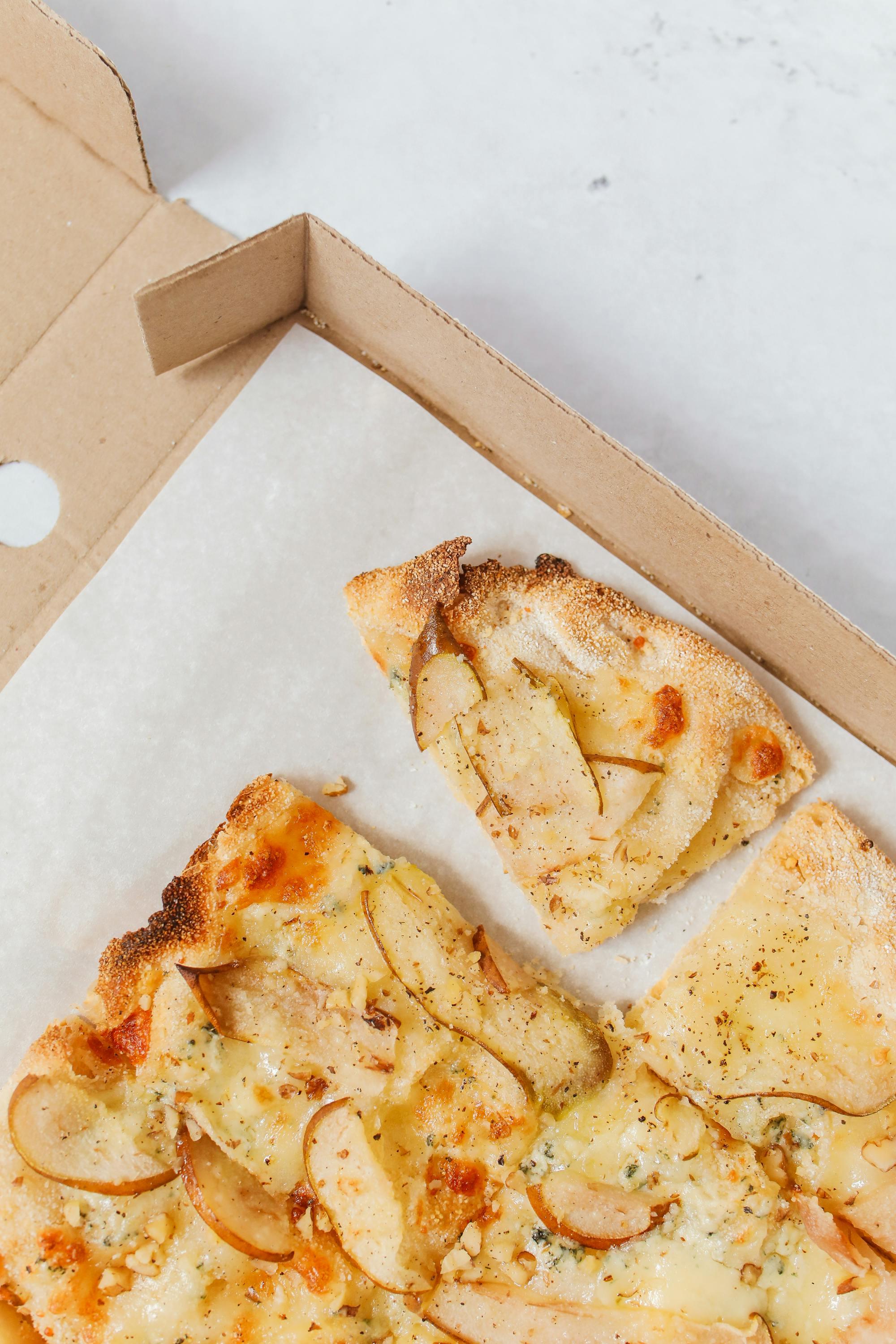 Delicious gourmet pizza with cheese and pear slices in a cardboard box, shot from above.