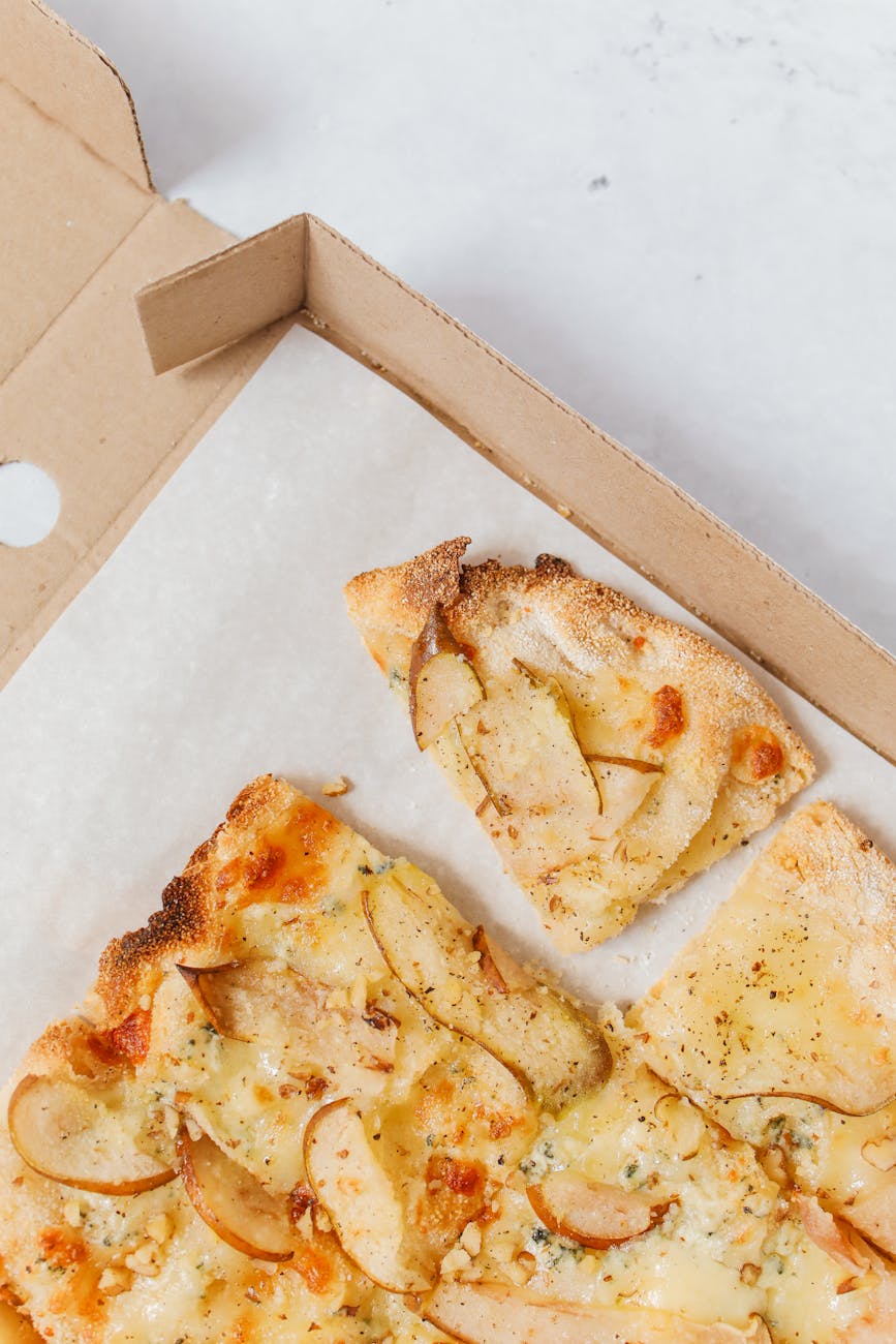 Delicious gourmet pizza with cheese and pear slices in a cardboard box, shot from above.