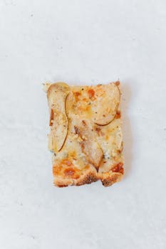 Close-up of a gourmet pizza slice topped with pears on a marble background.